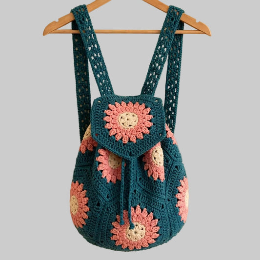 Wanderlust crochet backpack in teal with coral pink flowers, hanging on a hanger